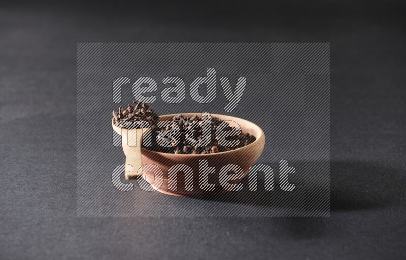 وعاء خشبي وملعقة خشبية ممتلئان بحبوب القرنفل على خلفية سوداء