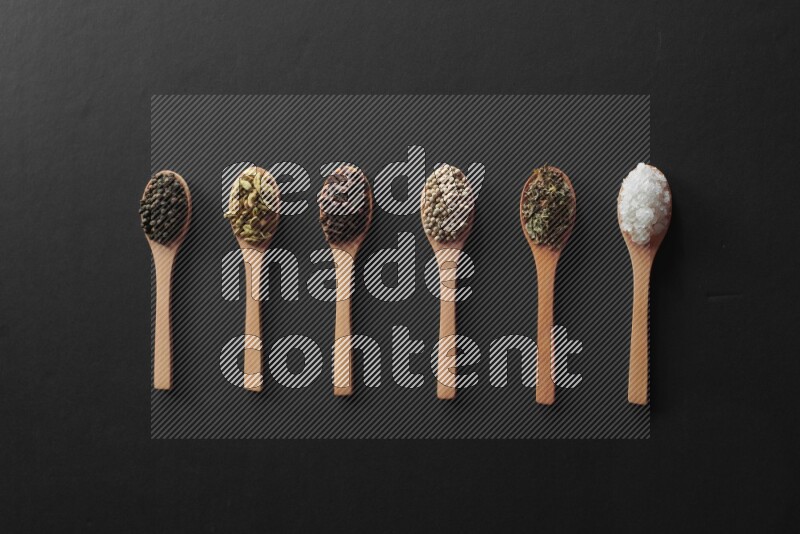 wooden spoons filled with white peppers, cloves, cardamom, salt, black peppers and basil on black flooring