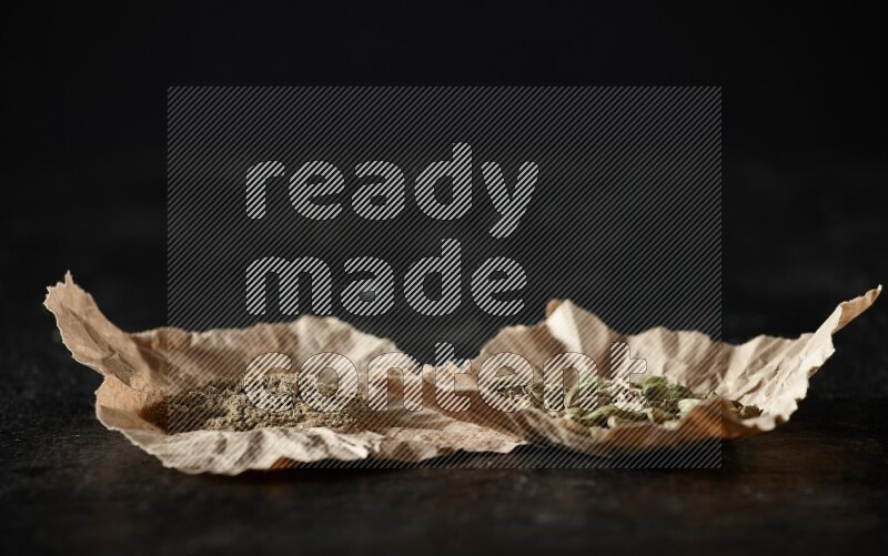 حبوب وبودرة الهيل في قطع من الورق على خلفية سوداء