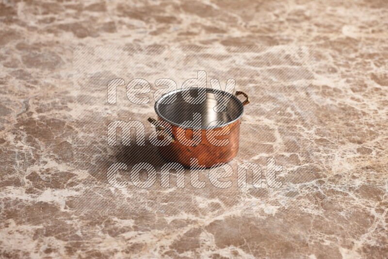 A small copper pot on beige marble background