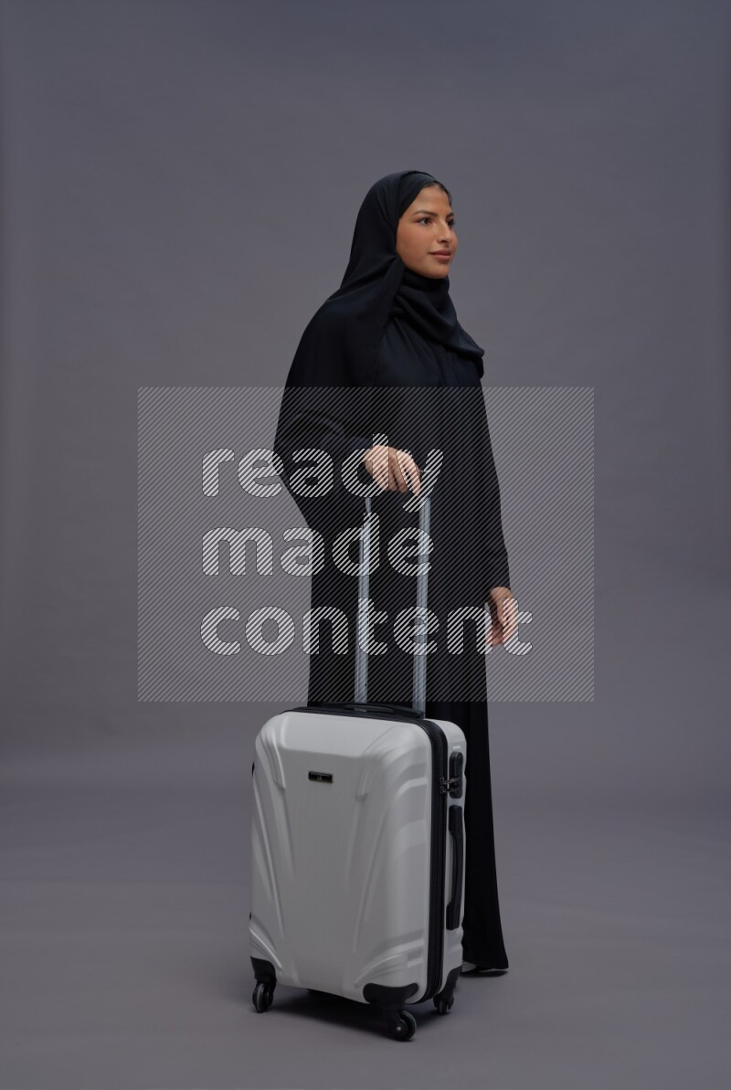 Saudi woman wearing Abaya standing holding bag on gray background