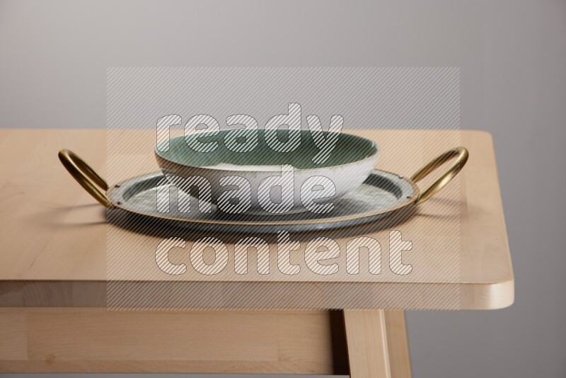 multicolored bowl placed on a rounded stainless steel tray with golden handels on the edge of wooden table