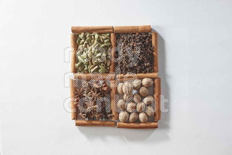 4 مربعات من أعواد القرفة ممتلئة بالهيل واليانسون والقرنفل وجوزة الطيب على أرضية بيضاء