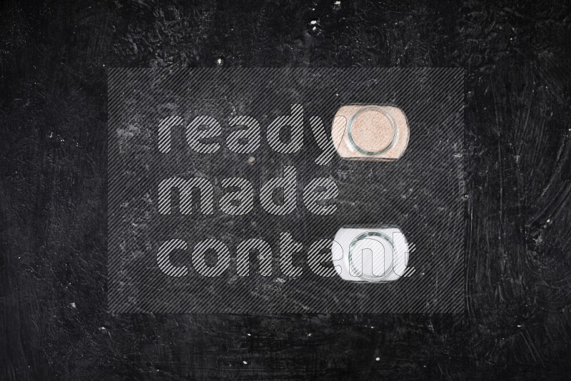 2 glass jars one is filled with fine himalayan salt and the other with table salt on black background