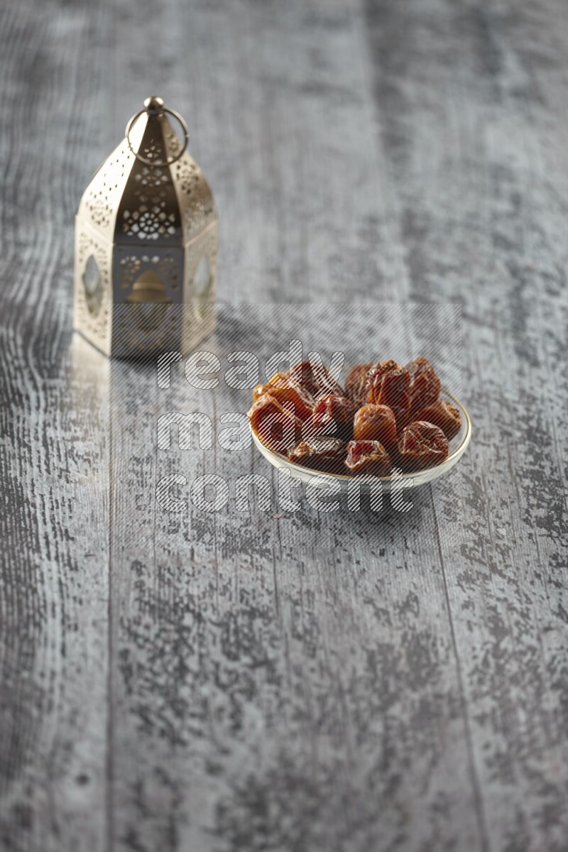 A silver lantern with different drinks, dates, nuts, prayer beads and quran on grey wooden background