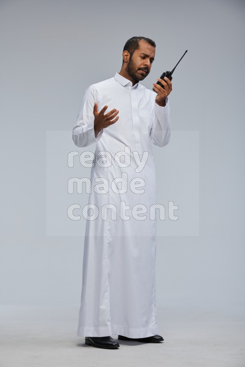Saudi man Wearing thob standing holding walkie-talkie on Gray background