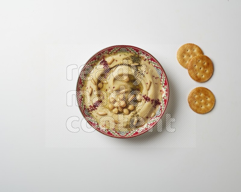 Hummus in a red plate with patterns garnished with zaatar & sumak on a white background