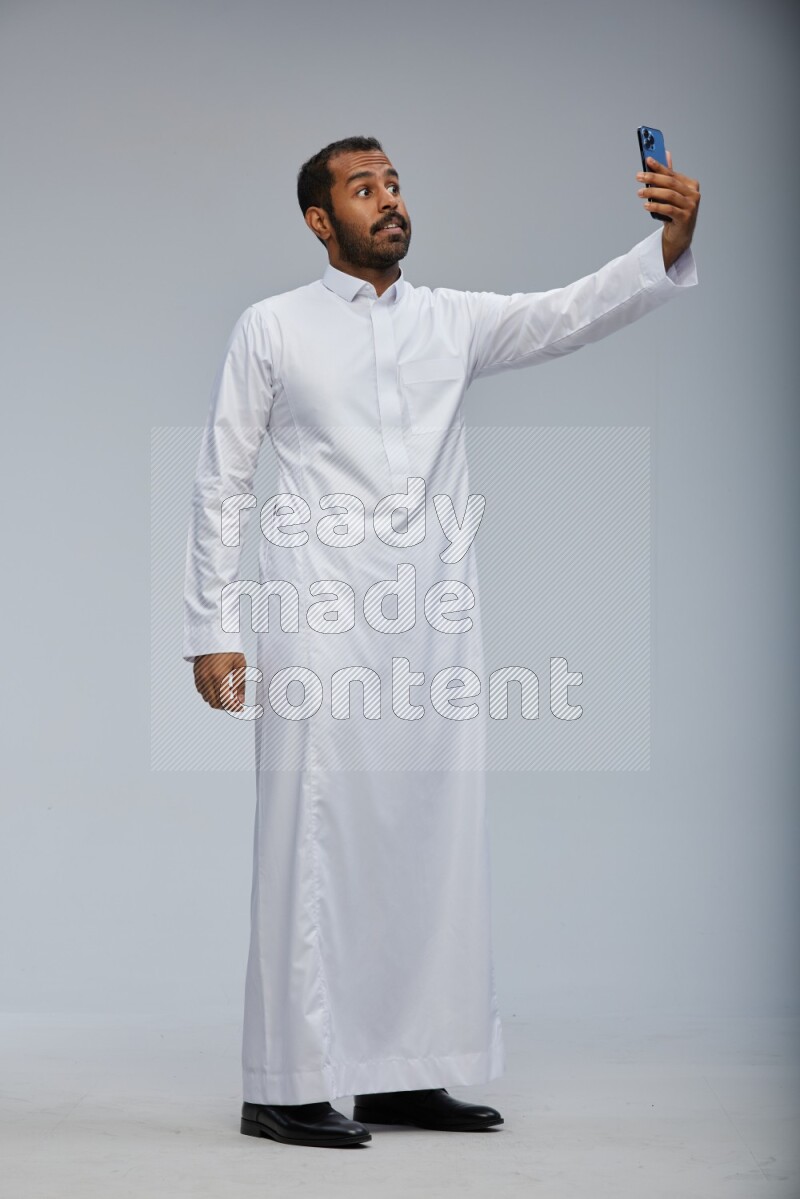 Saudi man wearing Thob standing taking selfie on Gray background