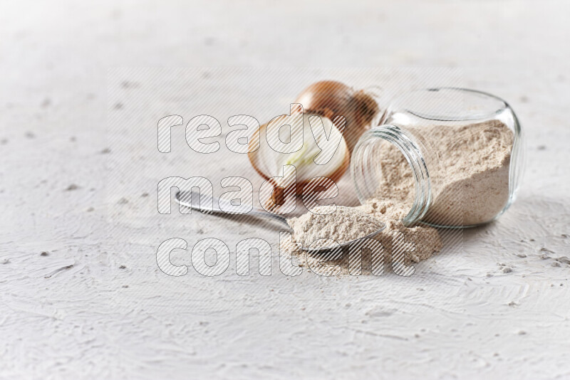 A glass jar full of onion powder flipped with some spilling powder on white background
