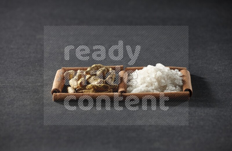 مربعان من أعواد القرفة ممتلئان بالملح الأبيض وأصابع الكركم علي خلفية سوداء