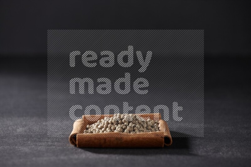 A single square of cinnamon sticks full of white pepper on black flooring