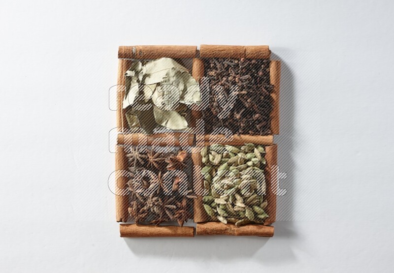 4 مربعات من أعواد القرفة ممتلئة بالهيل واليانسون والقرنفل وأوراق الغار على أرضية بيضاء