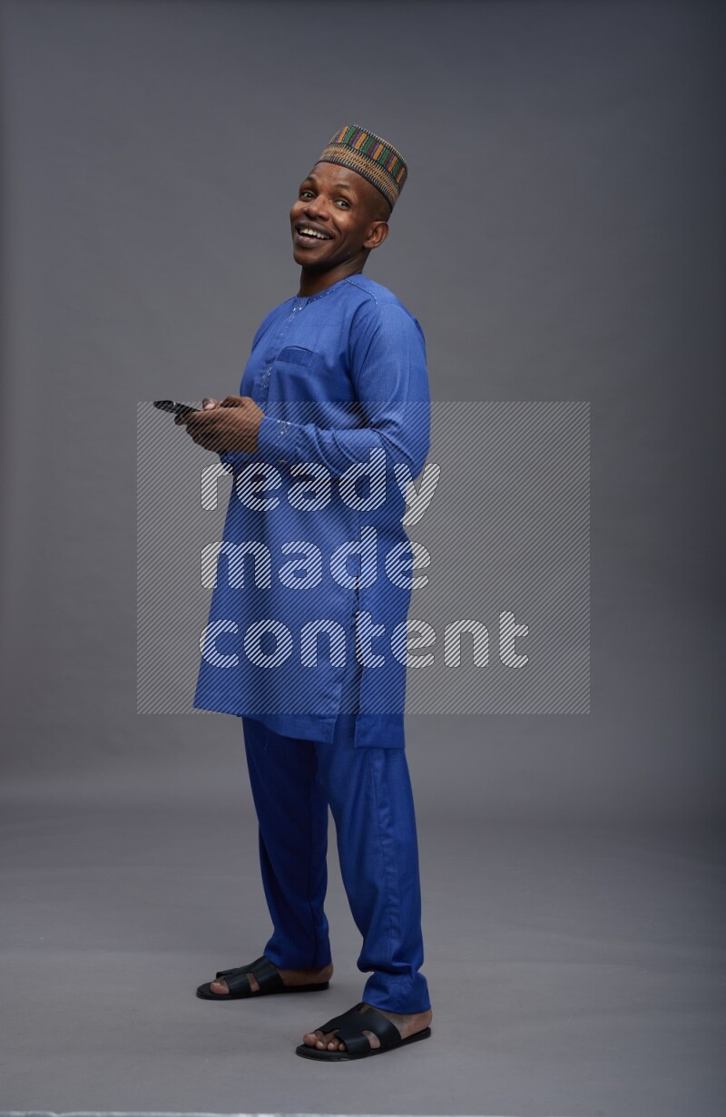 Man wearing Nigerian outfit standing texting on phone on gray background