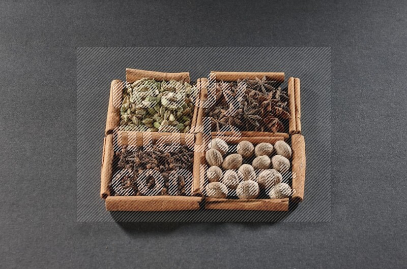 4 مربعات من عيدان القرفة ممتلئة بحب الهيل واليانسون النجمي وجوزة الطيب والقرنفل على أرضية سوداء