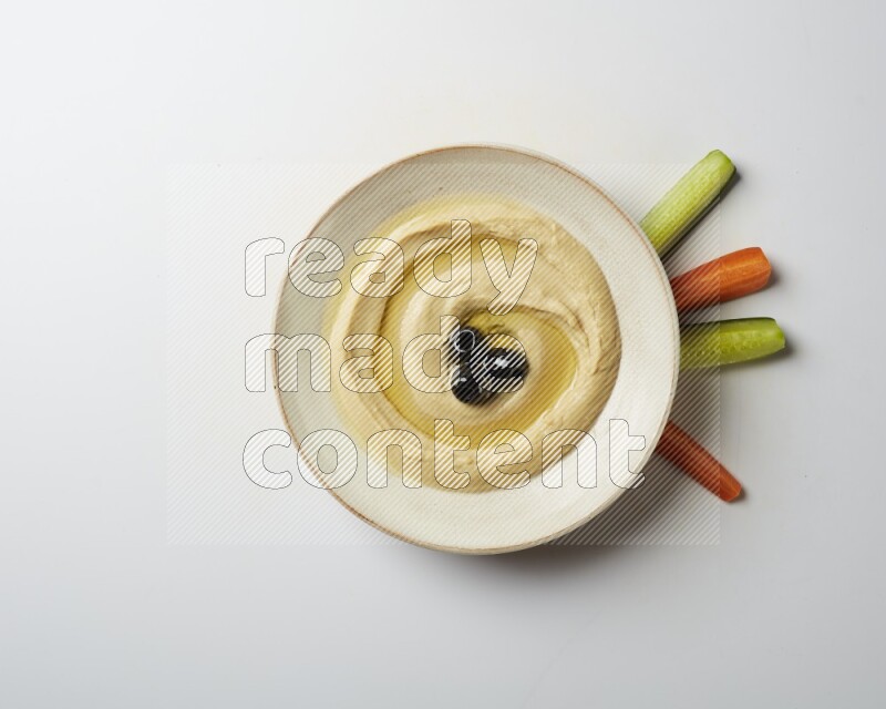 Hummus in a pottry plate garnished with black olives on a white background