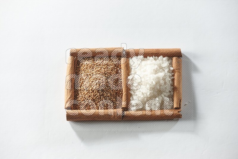 مربعان من أعواد القرفة ممتلئان بحبوب الخردل والملح الأبيض علي خلفية بيضاء