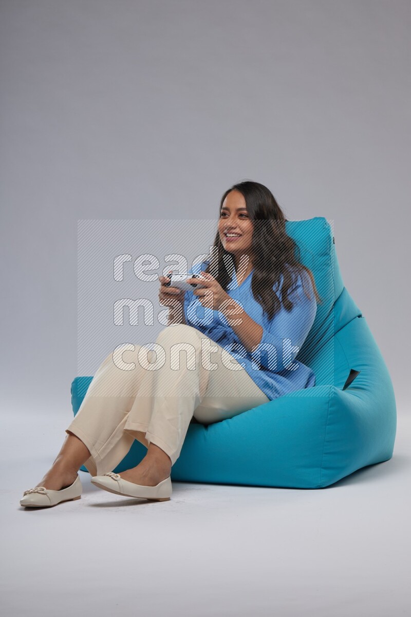 A woman sitting on a blue beanbag and gaming with joystick