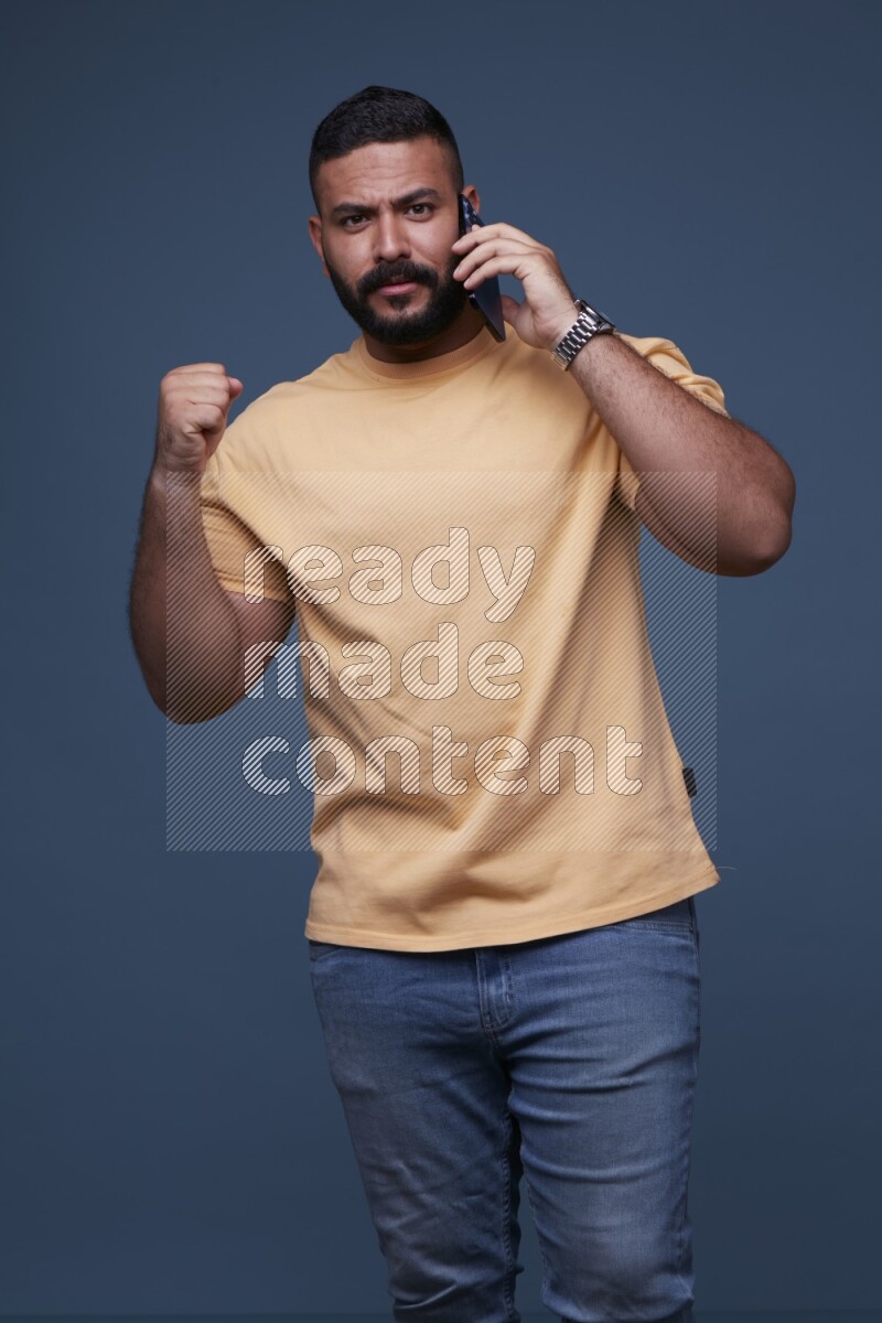 رجل يرتدي بنطال ازرق جينز وقميص اصفر بأكمام قصيره يتحدث بجواله