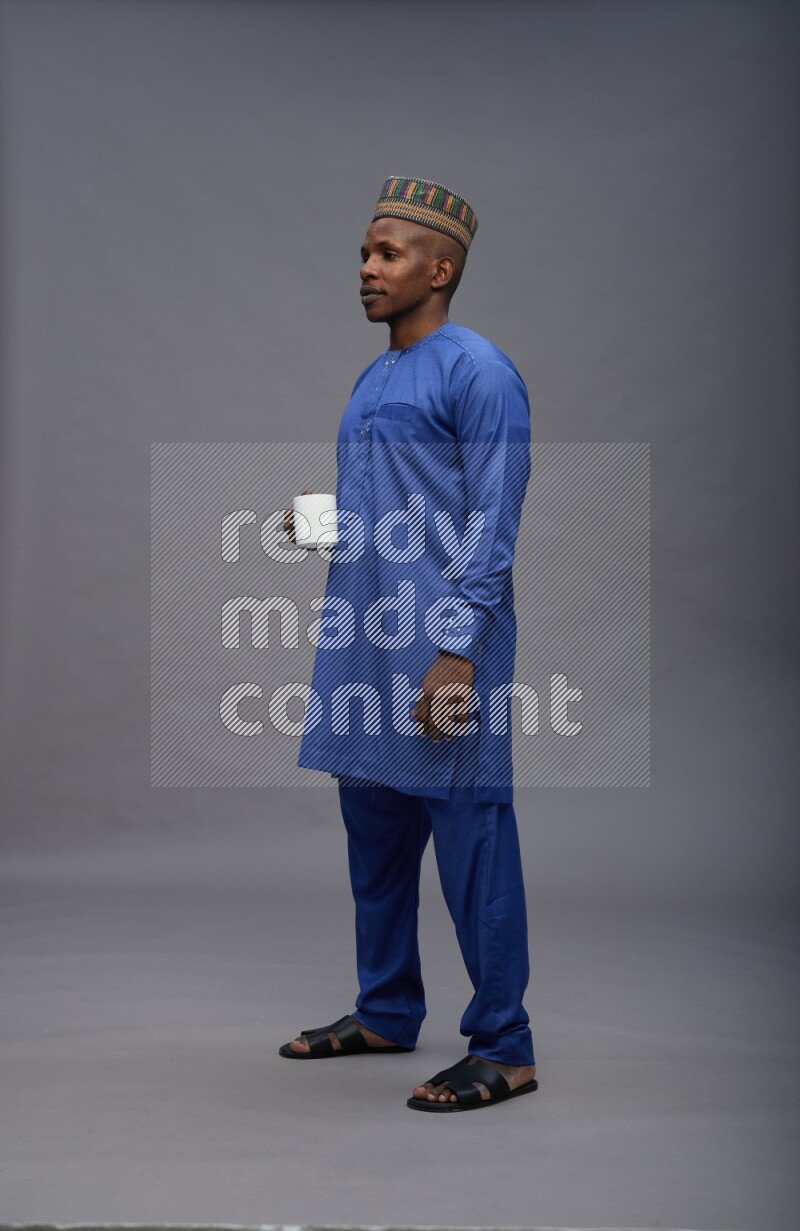 Man wearing Nigerian outfit standing holding mug on gray background