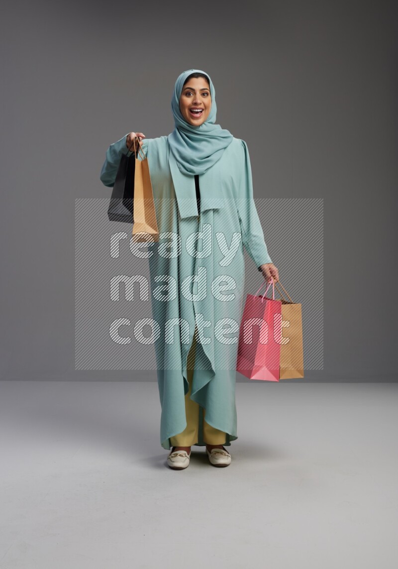 Saudi Woman wearing Abaya standing holding shopping bag on Gray background