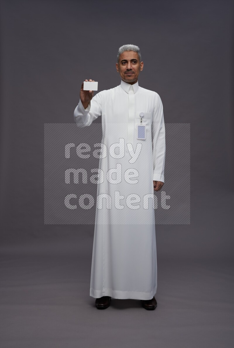 Saudi man wearing thob with pocket employee badge standing holding ATM card on gray background