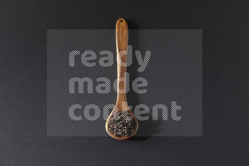 A wooden ladle full of whole cloves on a black flooring