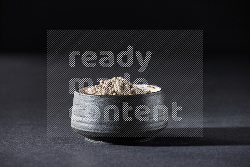 Black pottery bowl full of white pepper on black flooring