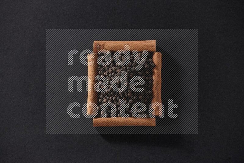 A single square of cinnamon sticks full of black pepper on black flooring