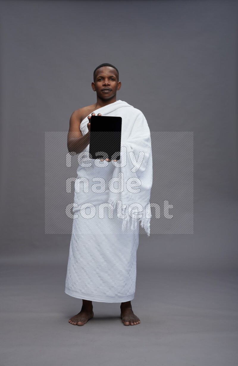 A man wearing Ehram Standing showing tablet to camera on gray background