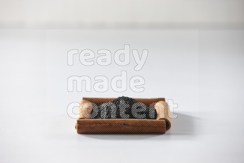 أربعة من أعواد القرفة مكونة شكل مربع بداخلها حبة البركة علي خلفية بيضاء