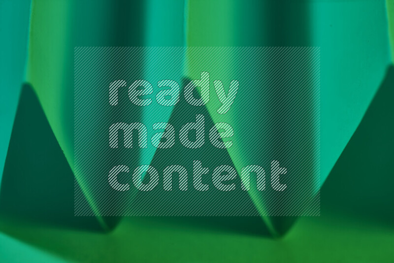 صورة مجردة مقربة تظهر طيات ورقية هندسية حادة بتدرجات اللون الأخضر