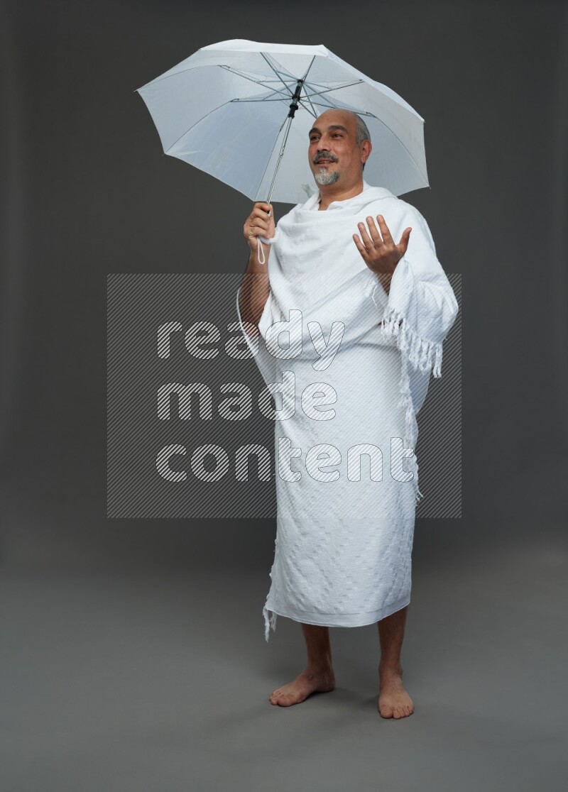 A man wearing Ehram Standing holding umbrella on gray background