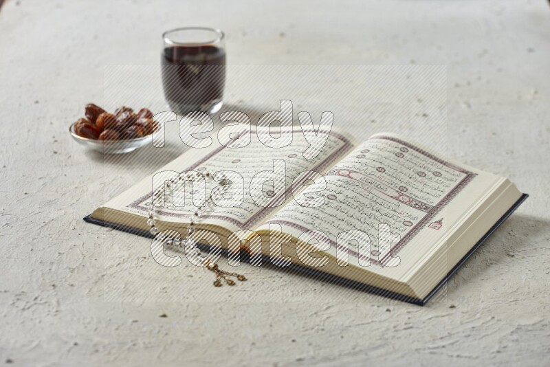 Quran with dates, prayer beads and different drinks all placed on textured white background