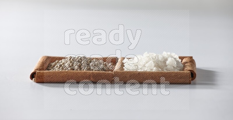 2 squares of cinnamon sticks full of white pepper and white salt on white flooring