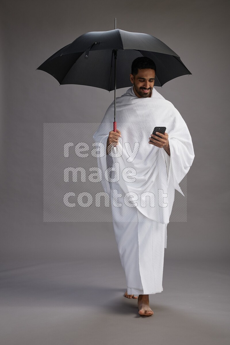 A man wearing Ehram Standing holding umbrella on gray background