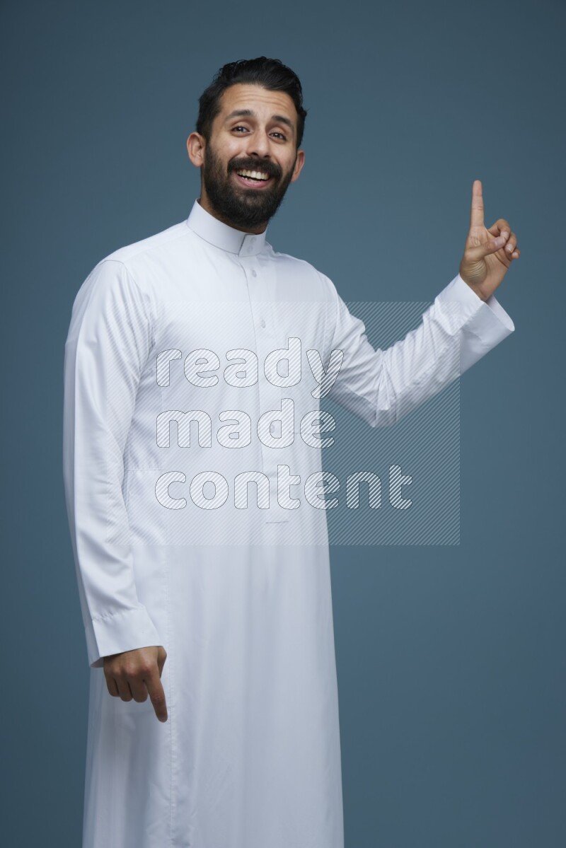 A man pointing in a blue background wearing Saudi Thob