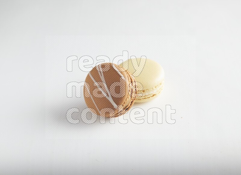 45º Shot of of two assorted Brown Irish Cream, and Yellow Vanilla macarons on white background