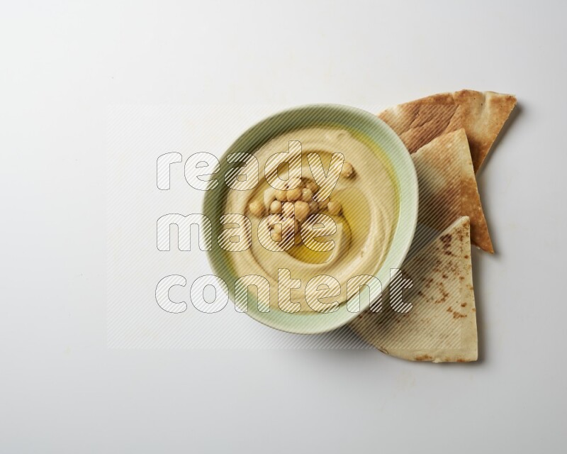 Hummus in a green plate garnished with roasted chickpeas  on a white background