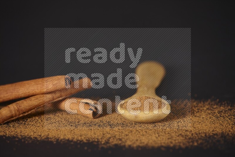 Cinnamon powder in a wooden spoon and cinnamon sticks beside it on black background