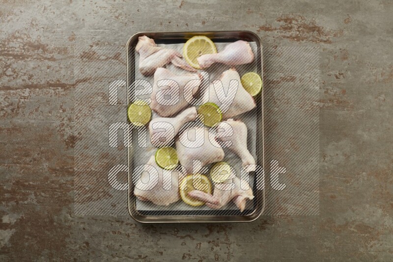 Mixed fresh chicken pieces in an oven tray on a textured rustic background