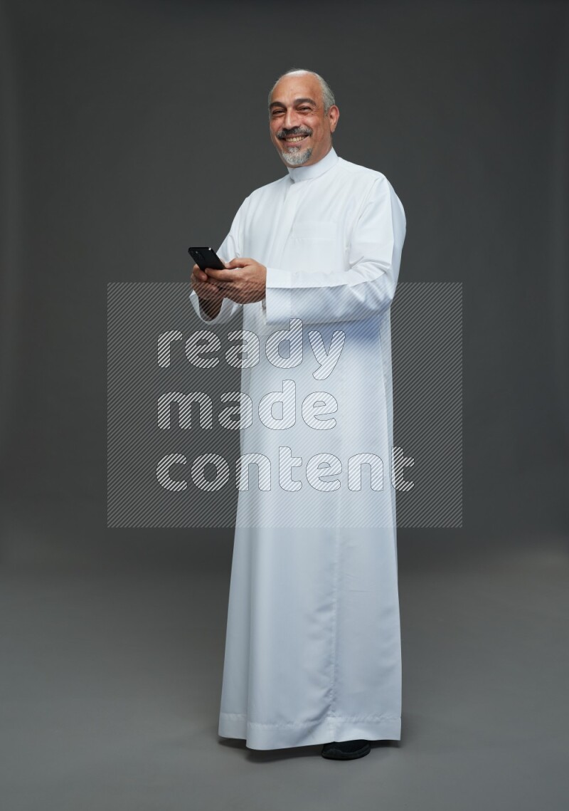 Saudi man without shomag Standing texting on phone on gray background