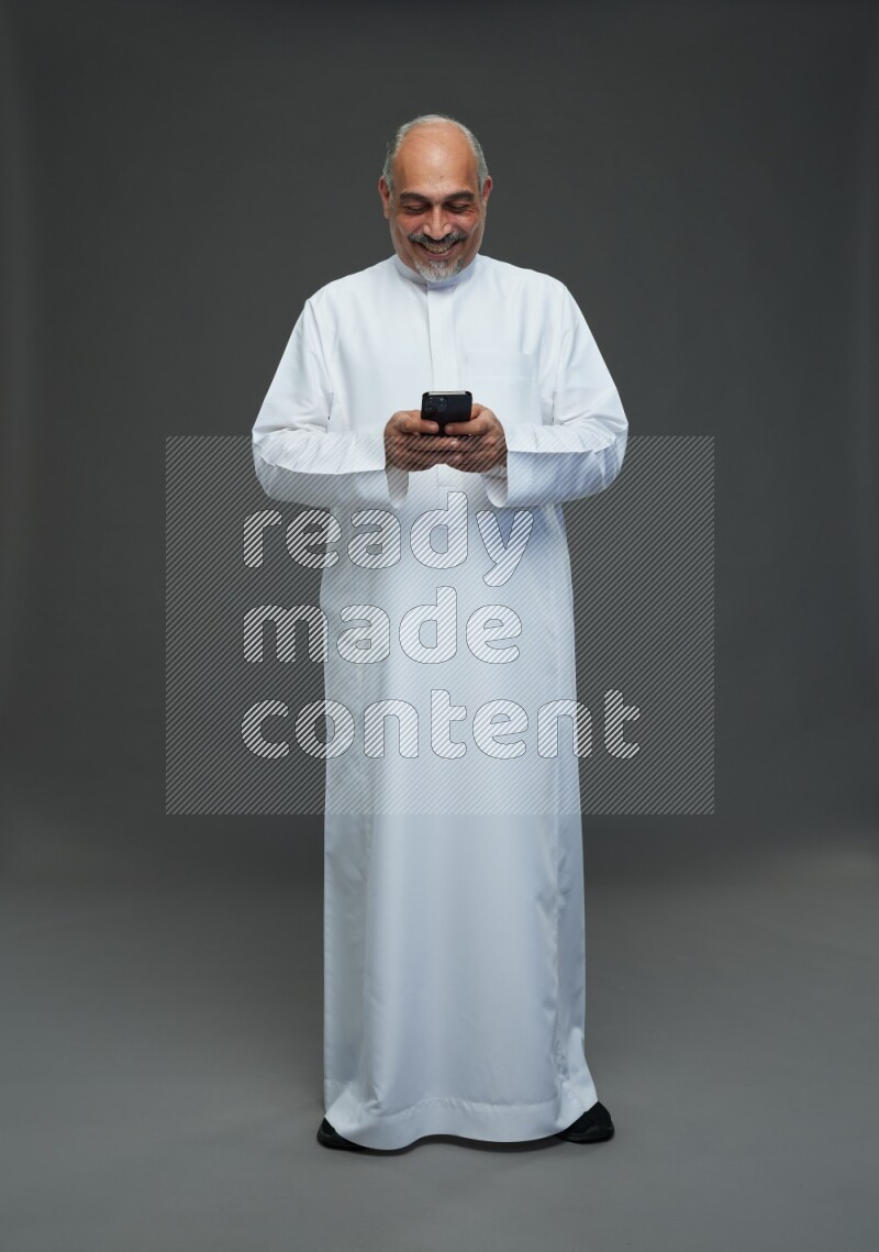 Saudi man without shomag Standing texting on phone on gray background
