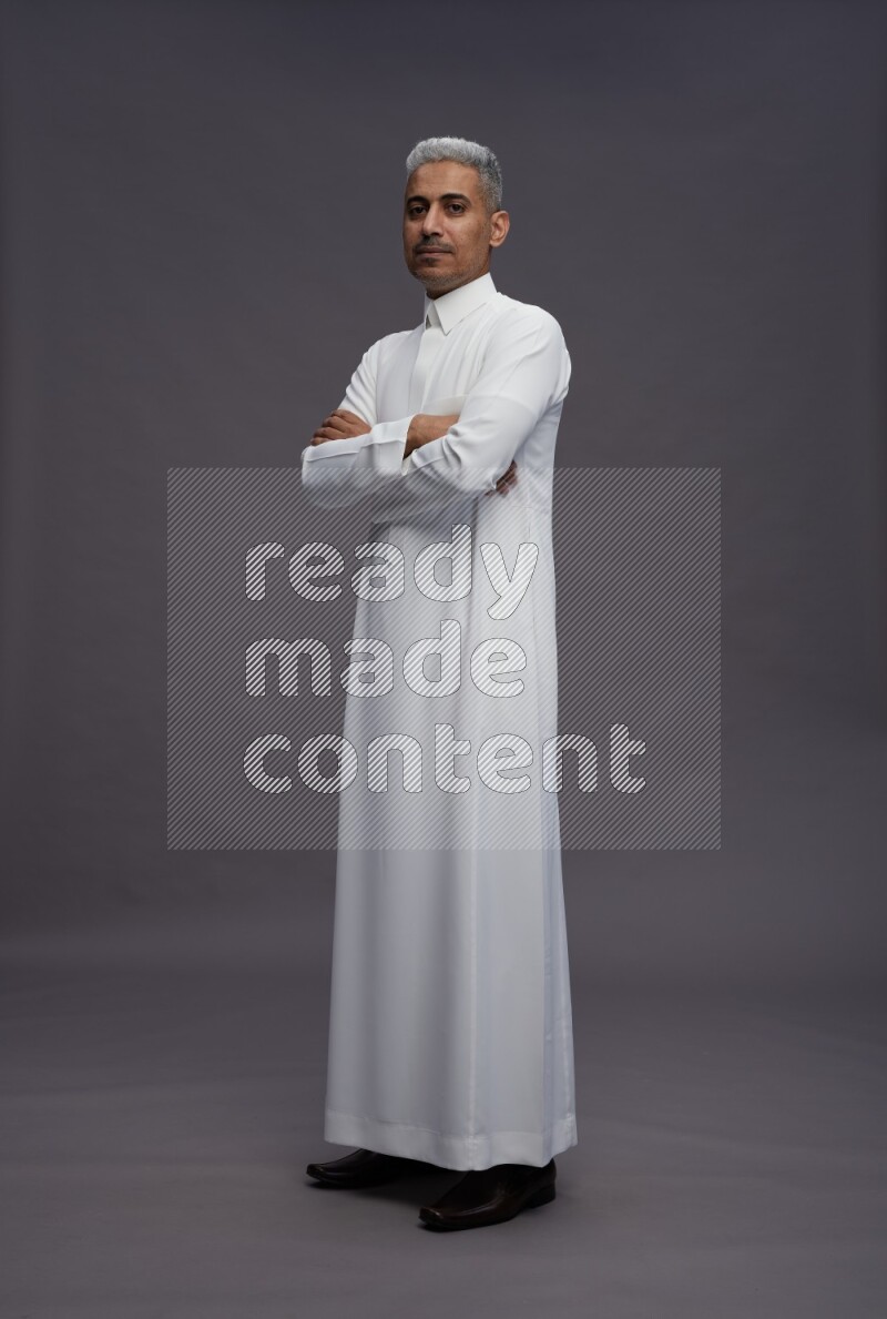 Saudi man wearing thob standing with crossed arms on gray background