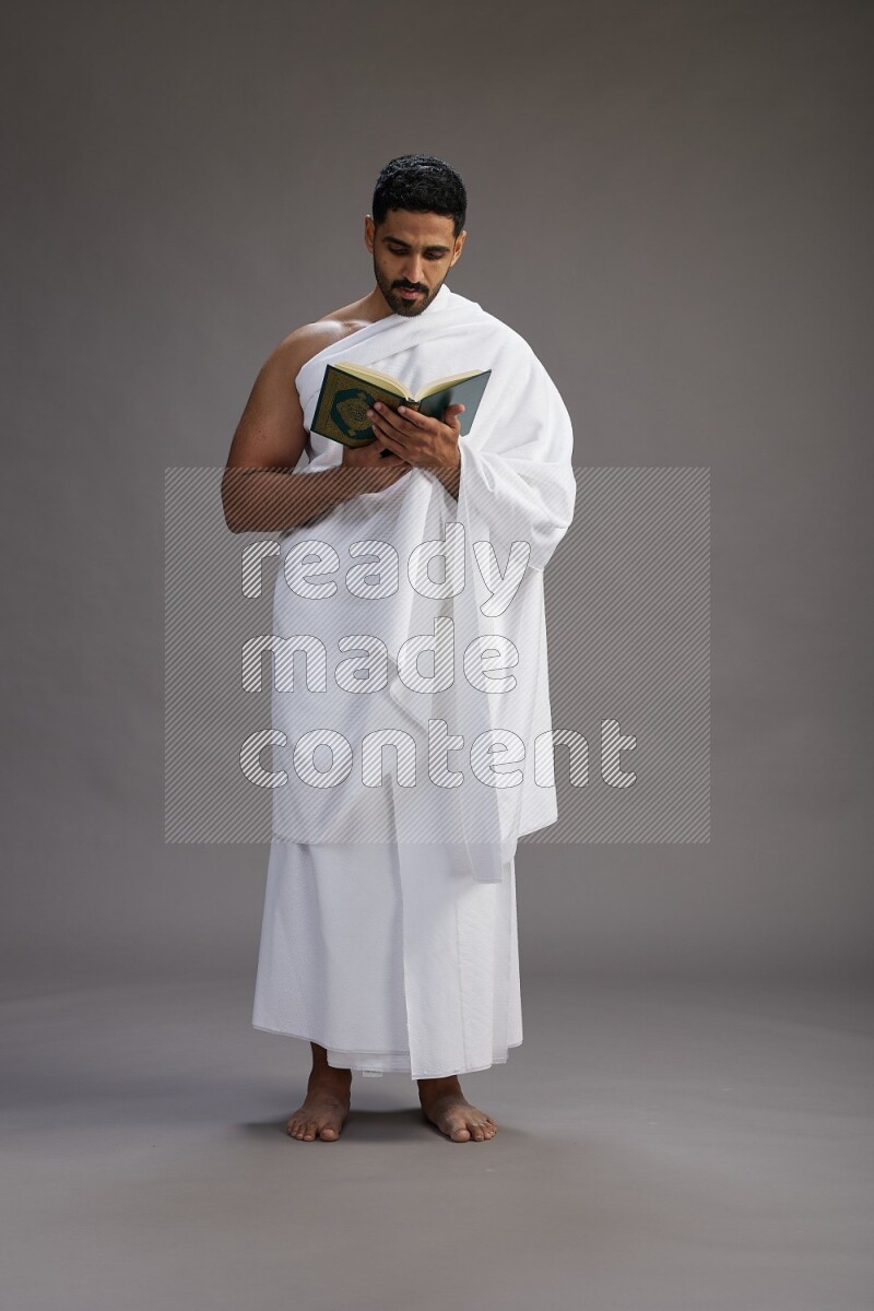 A man wearing Ehram Standing reading quran on gray background