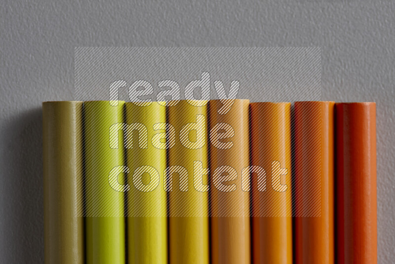 A collection of sharpened colored pencils arranged showcasing a gradient of yellow and orange hues on grey background