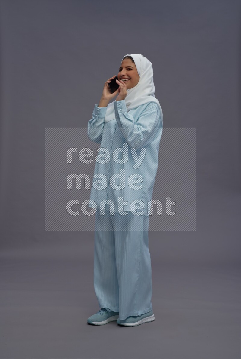 Saudi woman wearing hijab clothes standing talking on phone on gray background