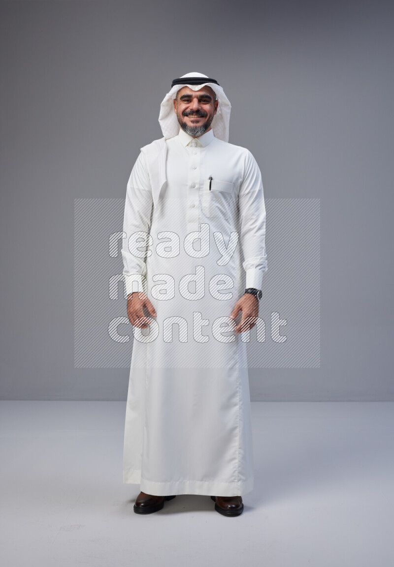 Saudi man Wearing Thob and white Shomag standing interacting with the camera on Gray background