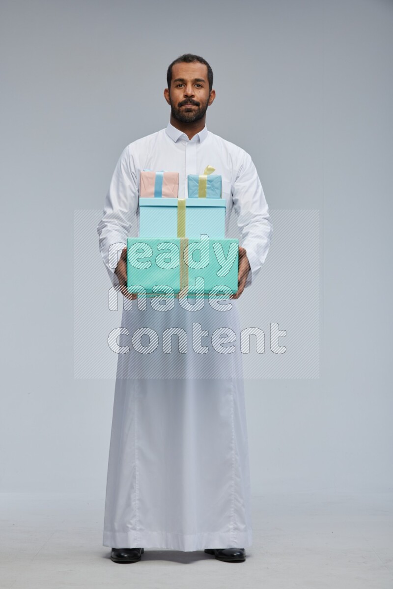 Saudi man Wearing thob standing holding gift box on Gray background