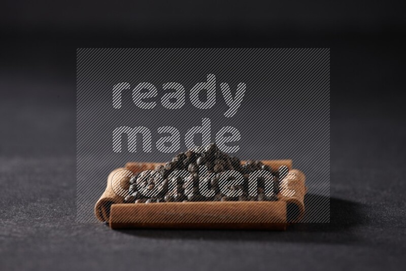 A single square of cinnamon sticks full of black pepper on black flooring
