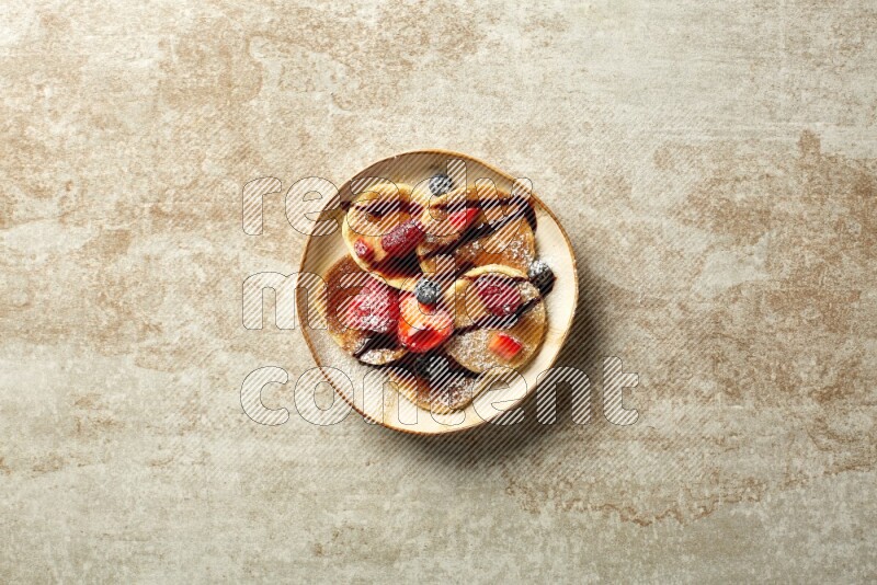 Five stacked mixed berries mini pancakes in an irregular plate on beige background